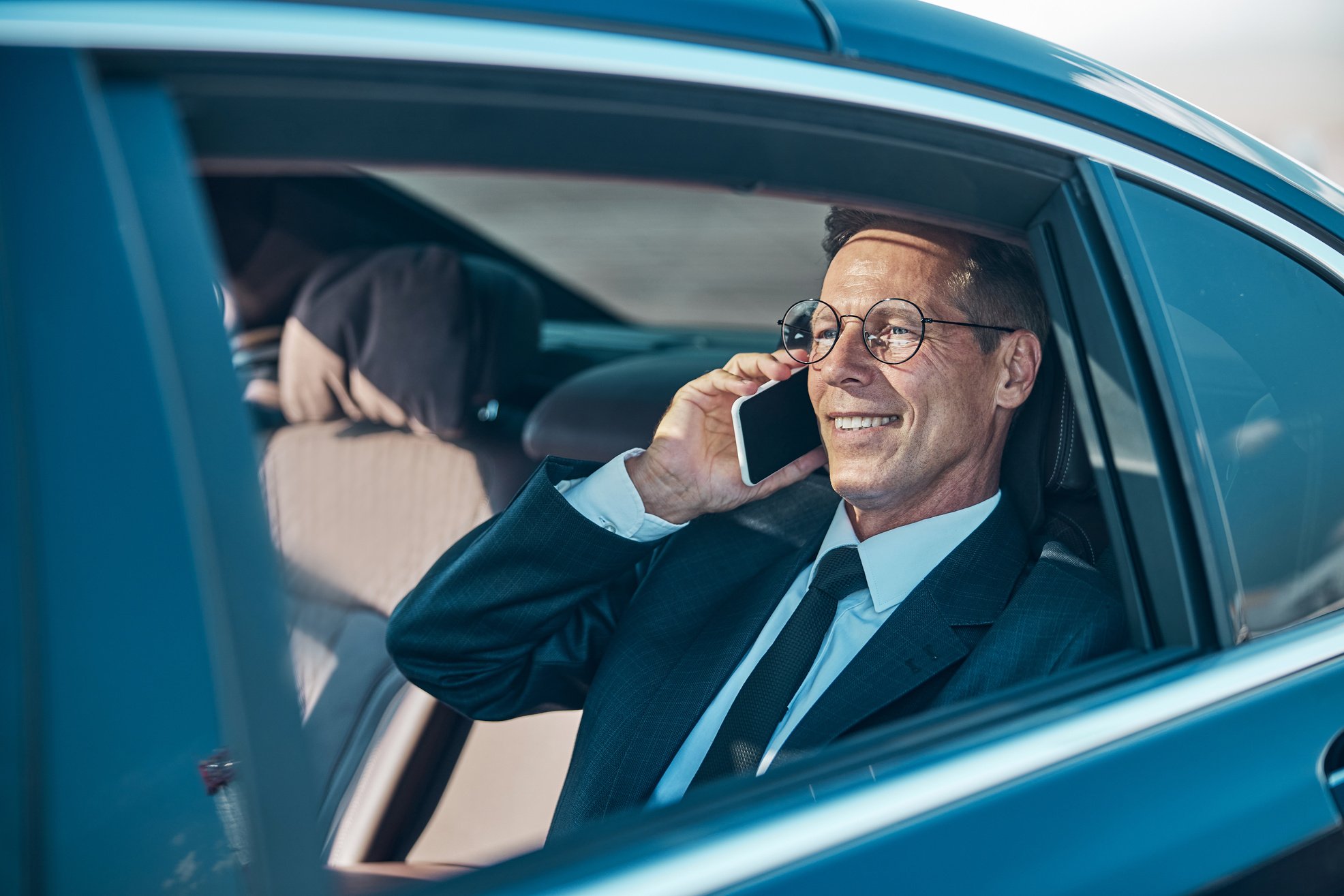 Cheerful businessman talking on smartphone during transfer from airport